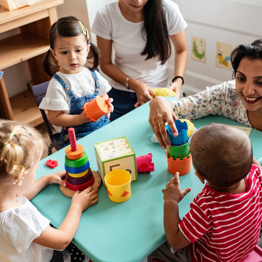 Nursery Children Playing With Teacher In The Classroom