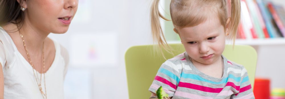 Child Girl Looks With Disgust At Healthy Vegetables. Mother Conv