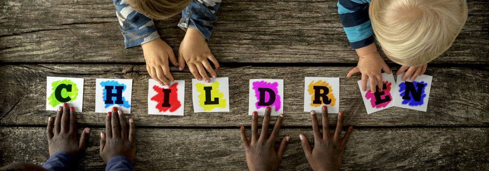 Top View Of Four Children Of Mixed Races Touching A Word Childre